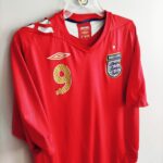 Wyjazdowa koszulka piłkarska reprezentacji Anglii z lat 2006-08 w kolorze czerwonym marki Umbro.