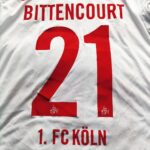Domowa koszulka 1. FC Koln (#21 L. Bittencourt) z sezonu 2017-18 w kolorze biało-czerwonym marki Erima.